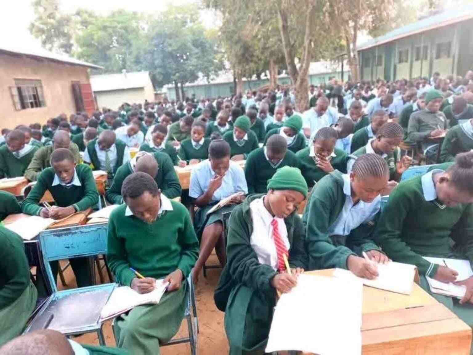 Students writing exams at outdoor desks on the grounds of Mwibale Senior School